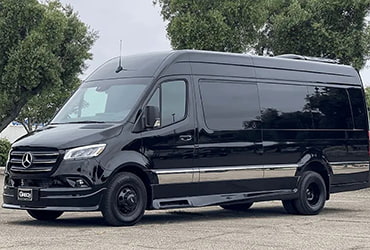 A black sprinter van on a tree-lined road